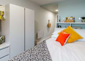 Thumbnail 23 of 51 - Bedroom with a bed and wardrobe. The bed is decorated with a grey throw, white bedding and orange/yellow pillows.