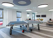 Thumbnail 3 of 48 - A ping pong table is in the middle of a room with a grey floor and white walls.