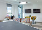 Thumbnail 4 of 48 - A ping pong table is in the middle of a room with two chairs and two TVs on the wall.