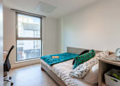 Thumbnail 6 of 48 - A bedroom with a bed, a chair, and a window overlooking a cityscape.
