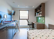 Thumbnail 12 of 48 - A bedroom with a bed, desk, and chair.