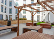Thumbnail 14 of 48 - A wooden pergola and benches are situated in a courtyard.