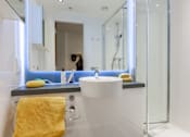 Thumbnail 34 of 48 - A woman is in a white bathroom with a yellow towel on a white chair.