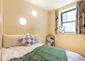 Thumbnail 32 of 35 - A bed with a green blanket and a blue and white pillow.