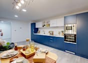 Thumbnail 11 of 21 - A modern kitchen with blue cabinets and a dining table set for a meal.