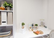 Thumbnail 14 of 21 - A white desk with a chair, a plant, and some stationery items.