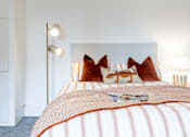 Thumbnail 3 of 59 - A bed with a white headboard and orange pillows with a white lamp on the side.