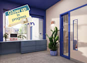 Thumbnail 7 of 21 - A sign that says "Glow up in progress" hangs over a desk in a room.
