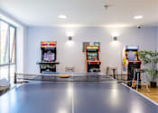 Thumbnail 3 of 35 - A ping pong table is in the middle of a room with arcade games on the wall.