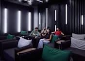 Thumbnail 4 of 41 - Four people sitting in a dark room with green pillows.