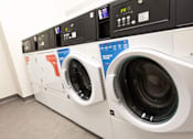 Thumbnail 23 of 23 - A row of washing machines with the front left one having a blue sticker on it.