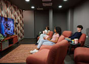 Thumbnail 4 of 36 - Four people are sitting in a room watching a movie on a large screen.