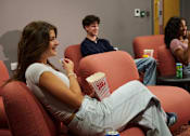 Thumbnail 13 of 36 - A woman is sitting on a red couch eating popcorn.
