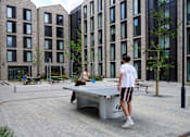 Thumbnail 16 of 36 - A man and a woman are playing ping pong in a courtyard.
