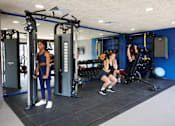 Thumbnail 33 of 36 - A woman is working out in a gym with a squat rack and a woman is doing squats.