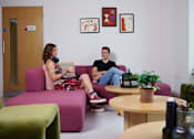 Thumbnail 11 of 36 - Two people sitting on a couch in a room with a plant on the table.