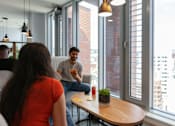 Thumbnail 18 of 51 - A man and a woman are sitting at a table in a bright room with large windows.