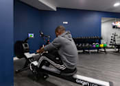 Thumbnail 37 of 51 - A man is working out on a rowing machine in a gym.