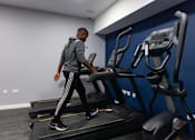 Thumbnail 39 of 51 - A man is walking on a treadmill in a gym.