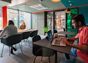 Thumbnail 6 of 51 - A man in a pink shirt is working on a laptop in a modern office space.