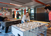 Thumbnail 2 of 51 - A man and a woman are playing foosball in a room with a ping pong table and other foosball tables in the background.