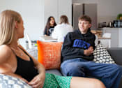 Thumbnail 20 of 51 - A young man in a black hoodie is sitting on a couch with a woman in a black tank top and a green skirt.