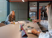 Thumbnail 4 of 51 - Two women having a conversation over a table with a can, glass of water, and a calculator on it.