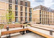 Thumbnail 25 of 56 - A modern building with a tree and benches in front.