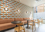 Thumbnail 32 of 56 - A room with a wall of patterned tiles and a row of chairs and tables.
