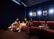 Thumbnail 15 of 73 - Three people are sitting in a room with red chairs and a blue wall.