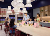 Thumbnail 56 of 73 - A group of people are gathered around a table in a room with hanging lights.