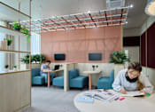 Thumbnail 42 of 73 - A woman is studying at a desk in a room with a pink wall and a wooden ceiling.