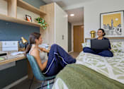 Thumbnail 18 of 73 - A woman is sitting on a bed with a laptop in front of her.