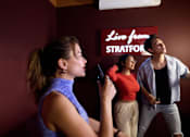 Thumbnail 36 of 73 - A woman is holding a microphone and singing while two other people watch her.