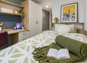 Thumbnail 12 of 56 - A bedroom with a bed, a desk, and a book on the bed.