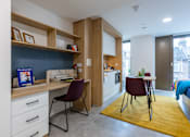 Thumbnail 16 of 56 - A room with a desk, chairs, and a kitchen area.