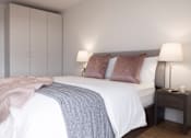 Thumbnail 8 of 10 - a bedroom with a white bed and a grey blanket and pillows