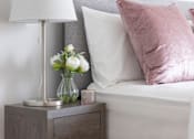 Thumbnail 5 of 10 - a bedroom with a bed and a nightstand with a lamp and flowers