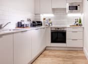 Thumbnail 9 of 23 - a white kitchen with a wooden floor and white cabinets