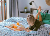 Thumbnail 2 of 14 - a woman laying in bed eating breakfast on her bed