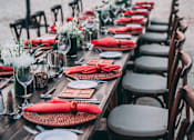 Thumbnail 11 of 20 - a long wooden table with red napkins and chairs at the beach