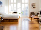 Thumbnail 9 of 14 - a bedroom with a bed and a living room with a wood floor