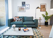 Thumbnail 16 of 23 - A living room with a green couch, a white coffee table, and a white lamp.