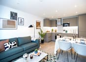 Thumbnail 2 of 23 - A modern living room with a grey sofa and a dining table set for two.