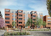 Thumbnail 12 of 23 - A modern apartment complex with red brick buildings and a courtyard with trees and people.
