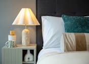 Thumbnail 25 of 37 - A white bed with a green pillow and a lamp on a nightstand.