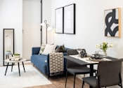 Thumbnail 22 of 25 - A modern living room with a blue couch, a black chair, and a dining table set for two.