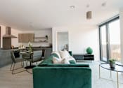 Thumbnail 14 of 30 - a living room with a green couch and a kitchen with a table and chairs at Vox Apartments, Manchester