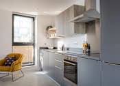 Thumbnail 15 of 30 - a kitchen with gray cabinets and a yellow chair at Vox Apartments, Manchester, M15 4YD