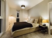 Thumbnail 15 of 24 - A bedroom with a bed, nightstand, and lamp.at Slate Yard Apartments, Salford, M3 5EX